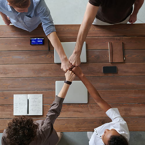 Fyra teammedlemmar sträcker in knytnävarna mot mitten - nu kör vi!