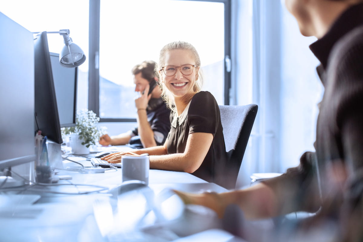 Glad IT-tjej med kollegor vid skrivbordet